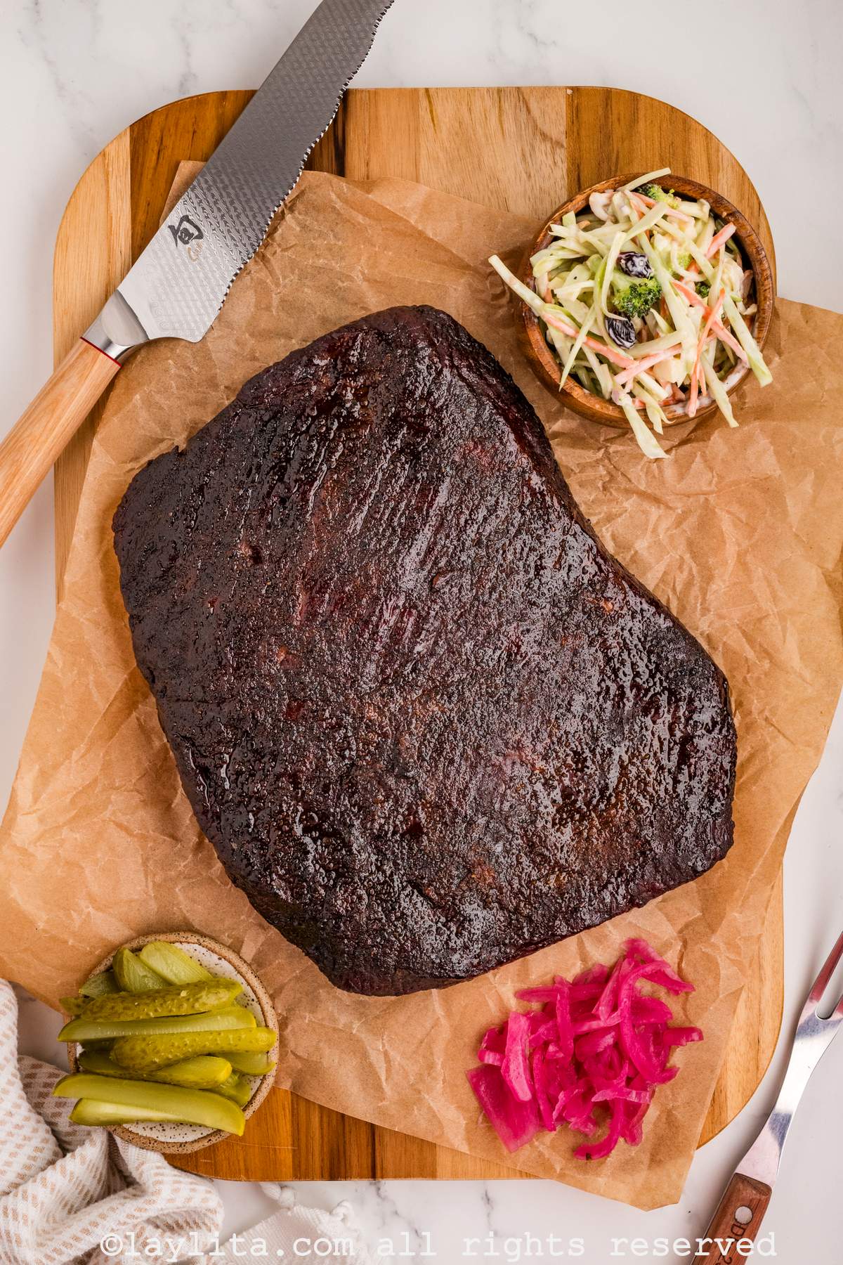 Overhead shot of finished brisket on a wooden board before cutting in with garnishes on the sides