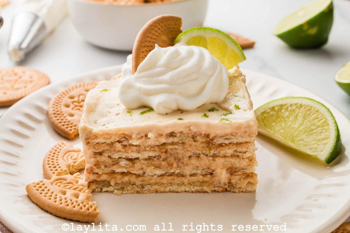 Side view of a slice of carlota de limón on a plate with some cookies and a lime wedge on the plate.