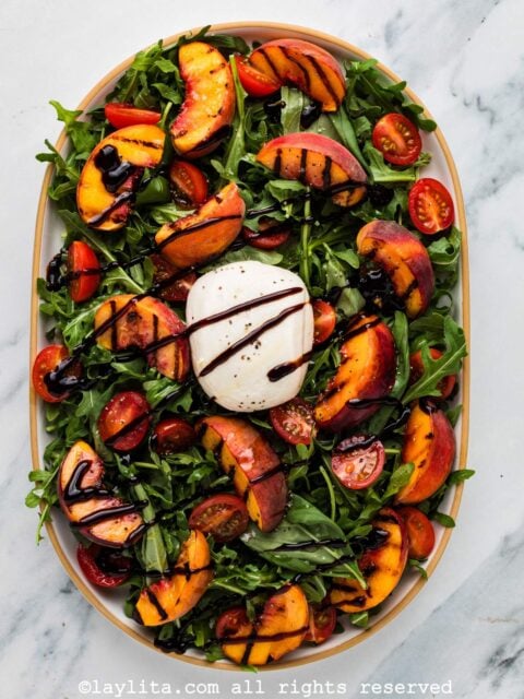Overhead view of a platter filled with grilled peach burrata salad drizzled with balsamic reduction