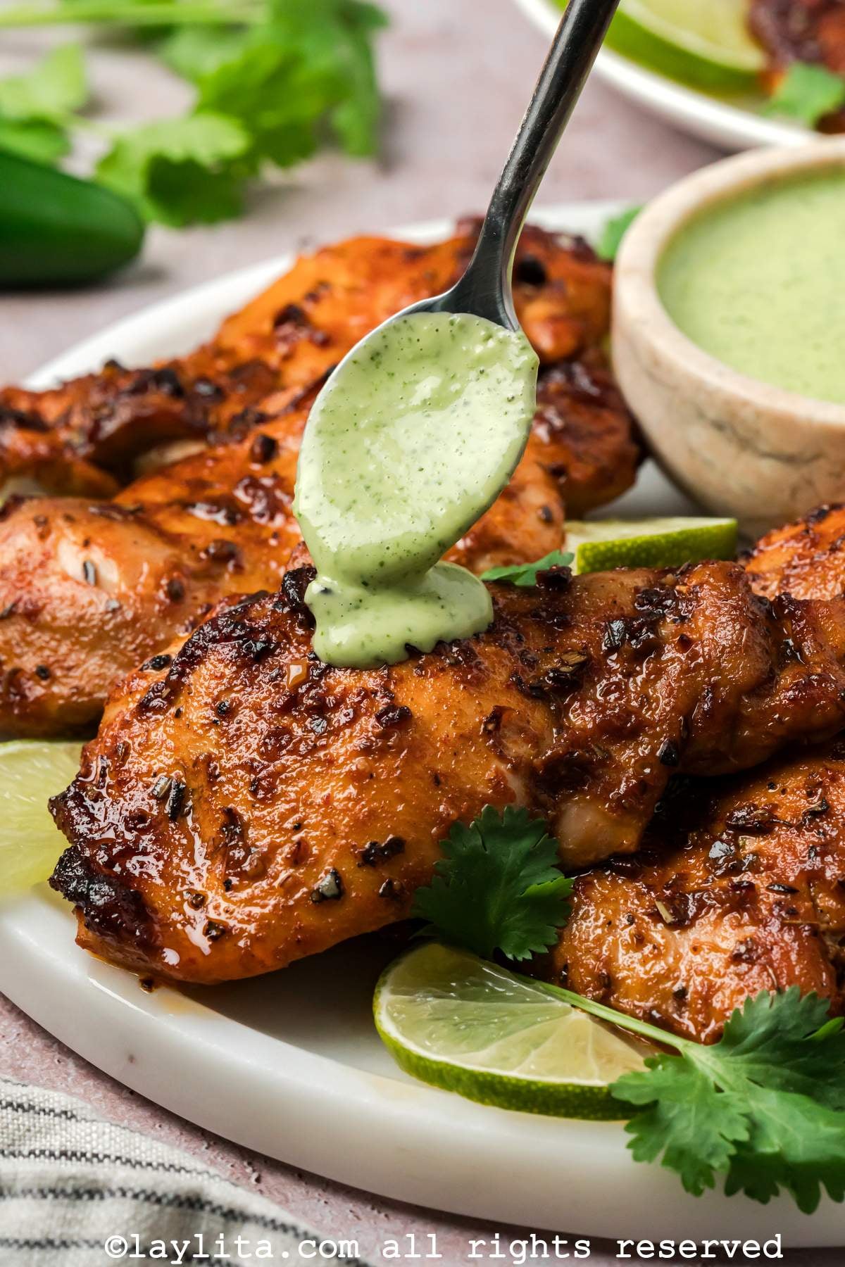 Spooning the green ají sauce on top of a Peruvian chicken thigh on a plate