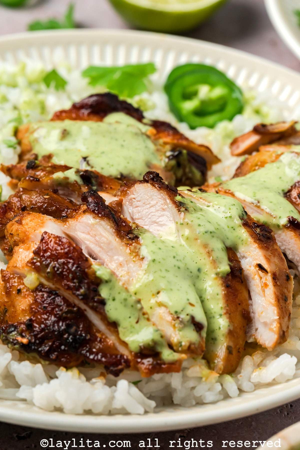 Sliced Peruvian chicken thighs on a bed of rice with green sauce on top