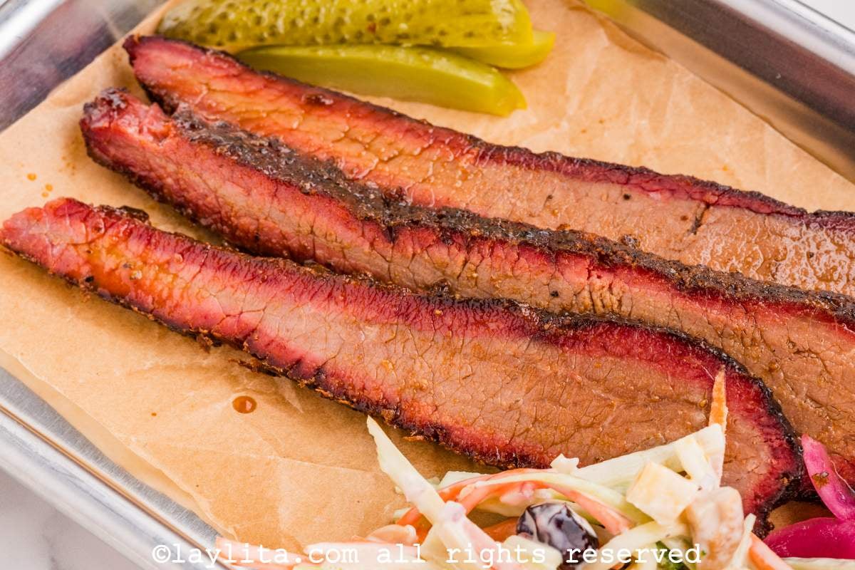 Close up of three slices of smoked brisket served with coleslaw and pickles