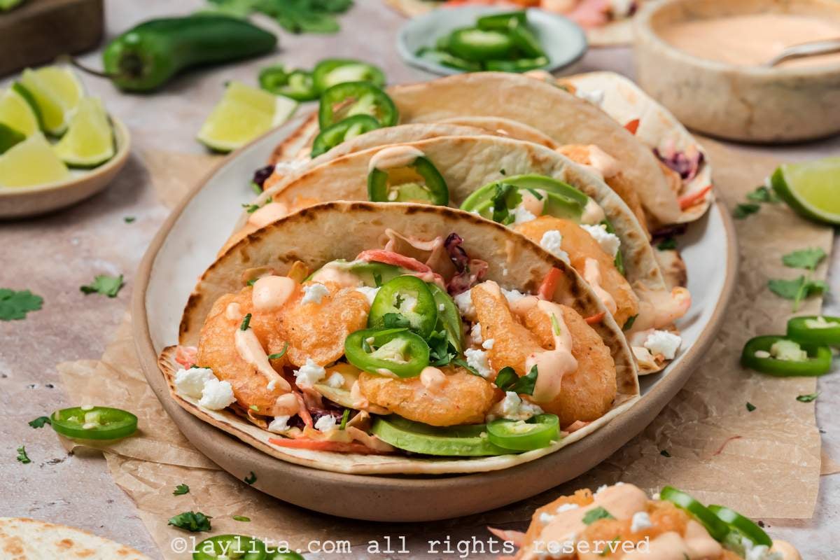 Side view of a platter of baja shrimp tacos surrounded by limes and fresh jalapeños.