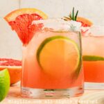 Side view of a paloma cocktail on a wooden board with a grapefruit wedge on the side.