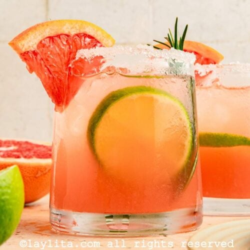 Side view of a paloma cocktail on a wooden board with a grapefruit wedge on the side.