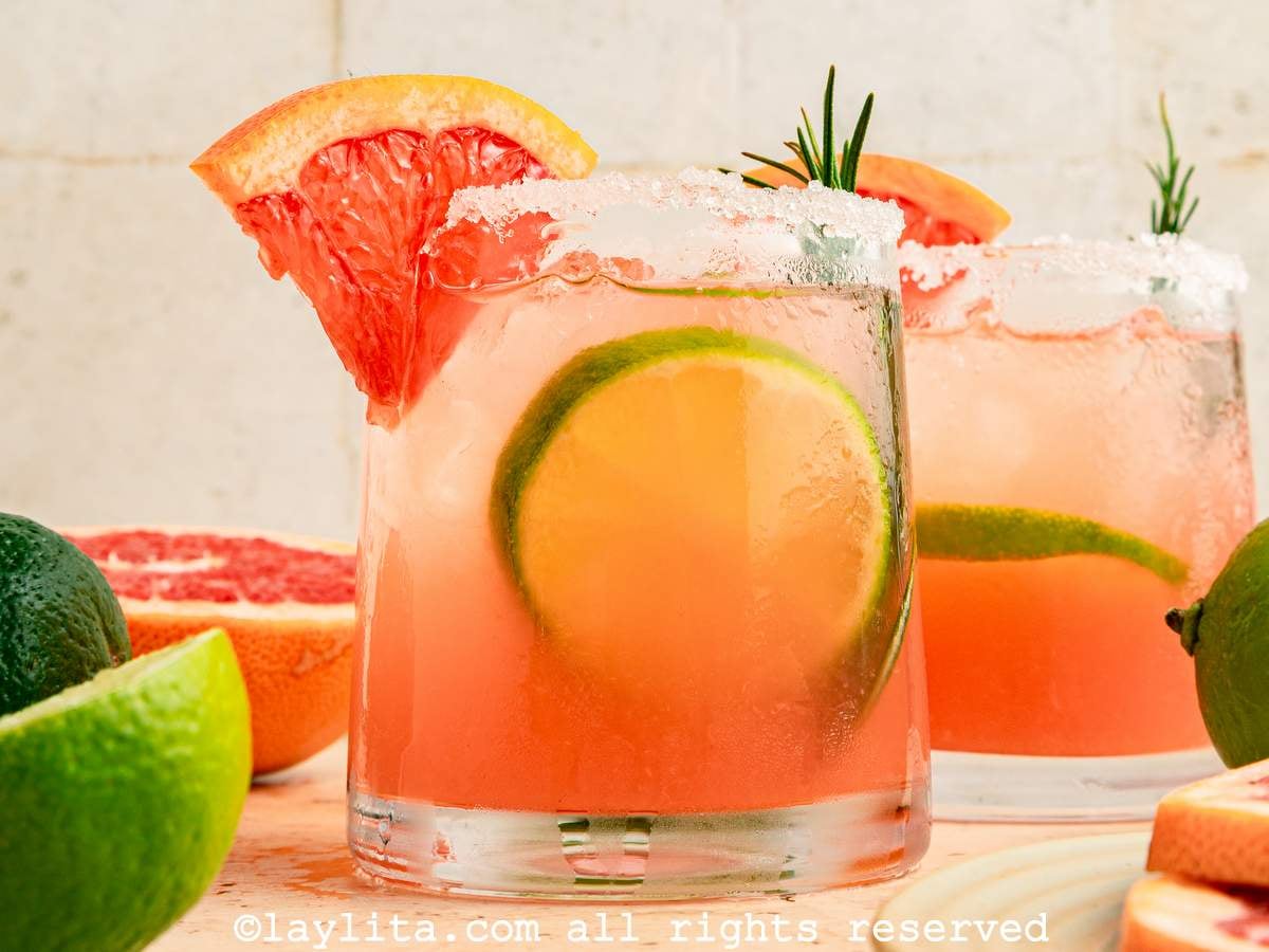 Side view of a paloma cocktail on a wooden board with a grapefruit wedge on the side.