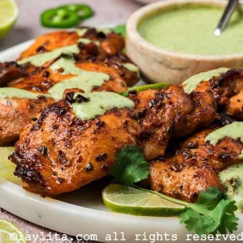 Side view of Peruvian chicken thighs on a plate next to a small bowl of green sauce or ají verde.