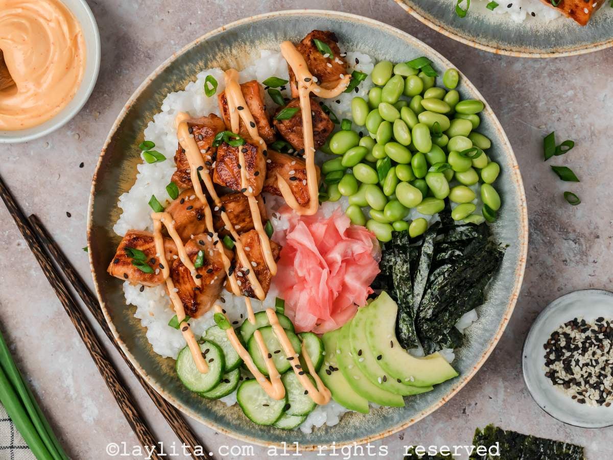 Overhead shot of a sushi bowl with rice, salmon bites, cucumbers and a spicy mayo drizzle on top.