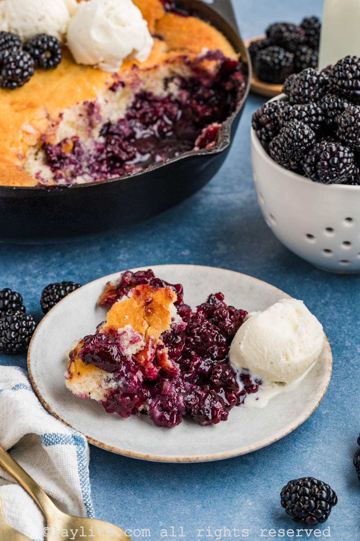 Blackberry cobbler served on a plate with ice cream on the side and the rest of the cobbler in the background