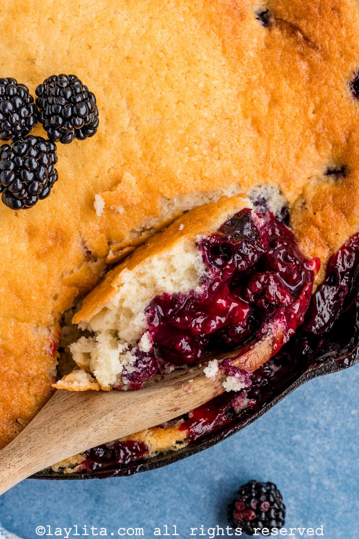 Wooden spoon scooping up some blackberry cobbler from a skillet.