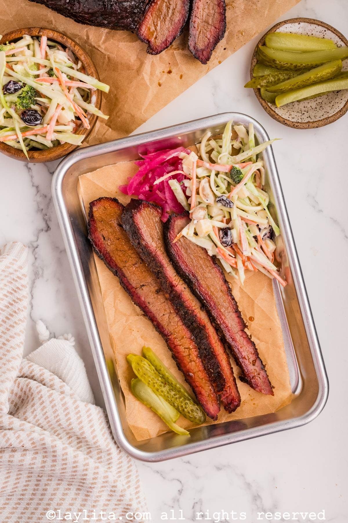 Smoked brisket slices served on a small sheet pan with coleslaw and pickles on the side.