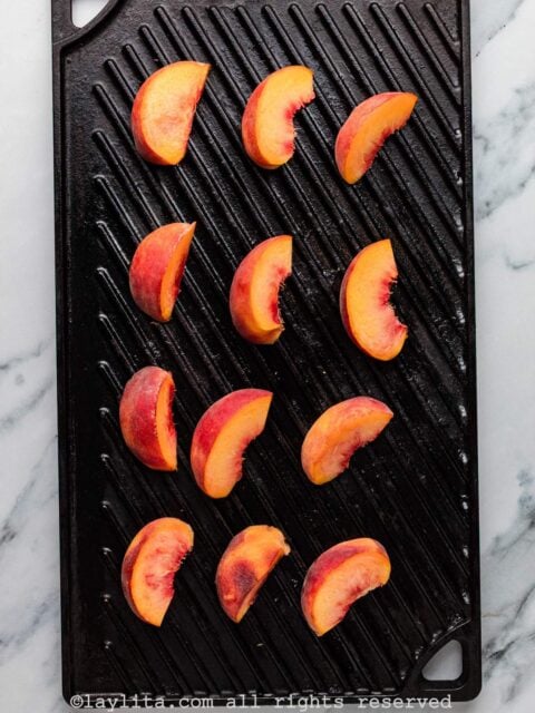 Several peach slices on a cast iron grill plate
