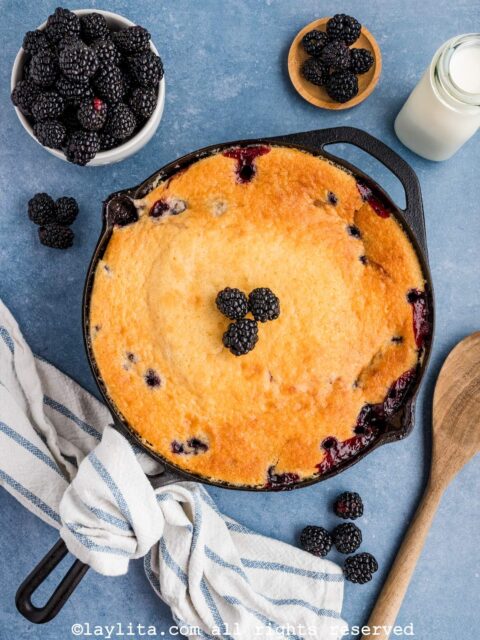 Overhead view of a baked blackberry cobbler in a skillet with berries on top and on the sides