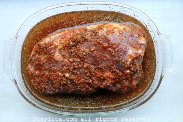 A pork shoulder marinating in a glass baking mold