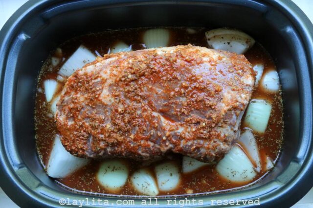Pork shoulder on top of onions and garlic in a slow cooker before cooking