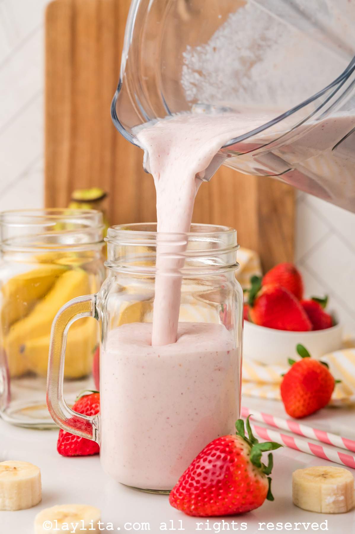 Pouring a strawberry banana milkshake from the blender into a glass jar.