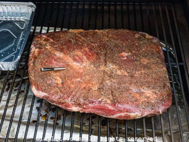 A beef brisket in the smoker next to a container with water