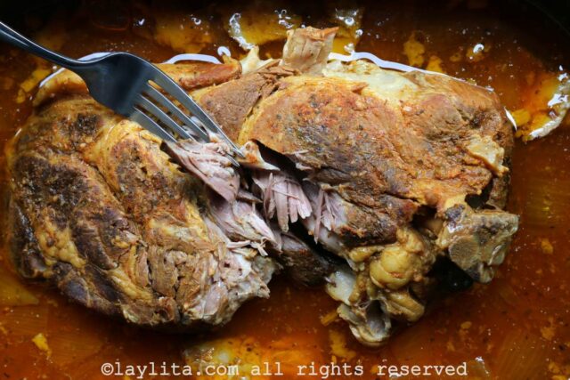 Pork shoulder in a slow cooker after cooking showing the tender pork being pulled with a fork