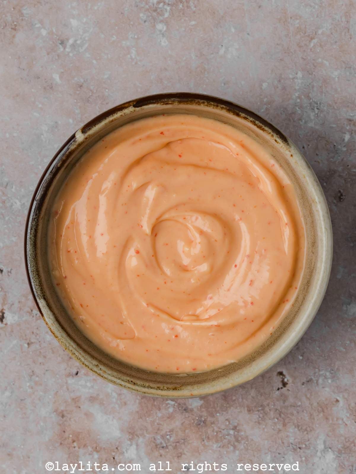 Overhead view of a bowl of spicy mayo on a concrete counter