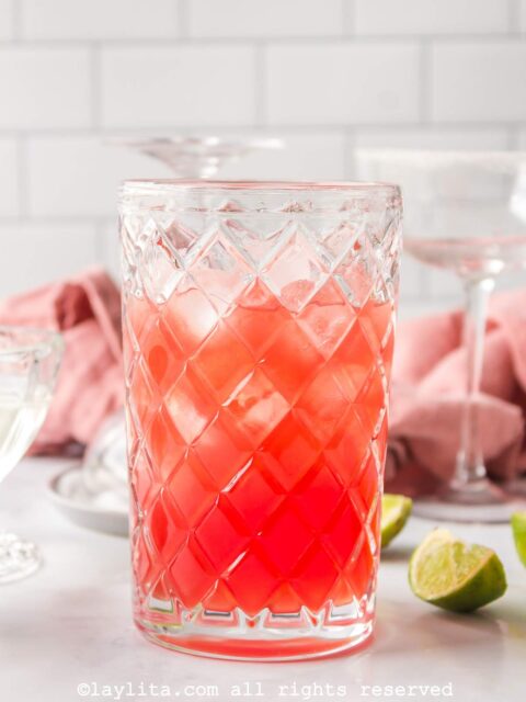 Side view of a glass shaker with the ingredients for watermelon margarita in it.