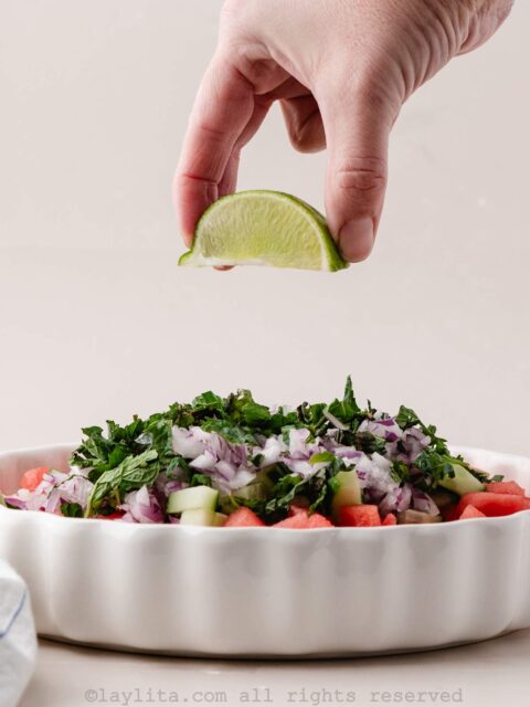 A hand squeezing a lime wedge over a watermelon salad