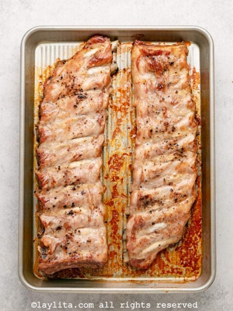 Two racks of pork ribs on a baking tray after baking
