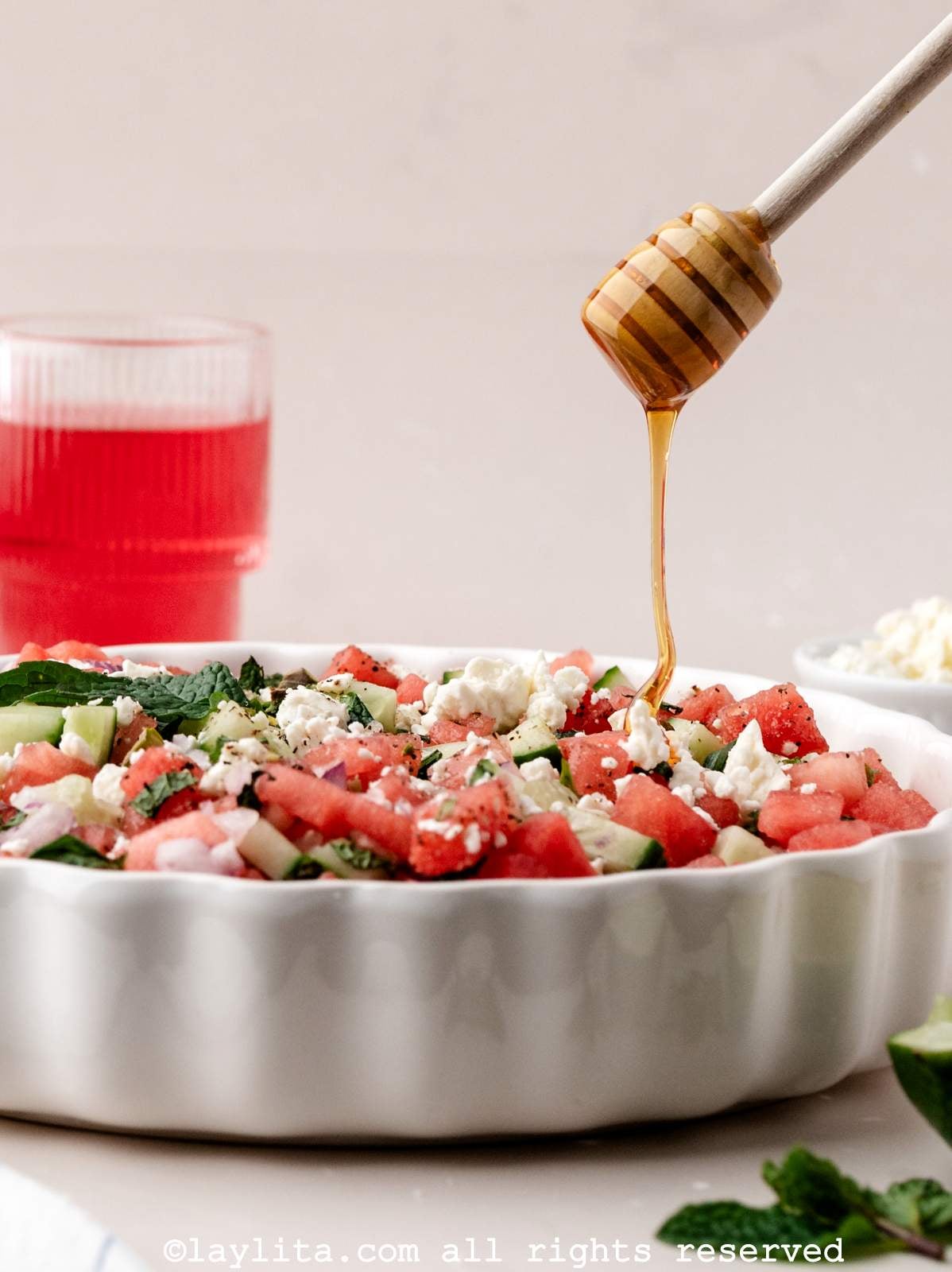 Side view of a a bowl of watermelon feta salad with honey being drizzled on top