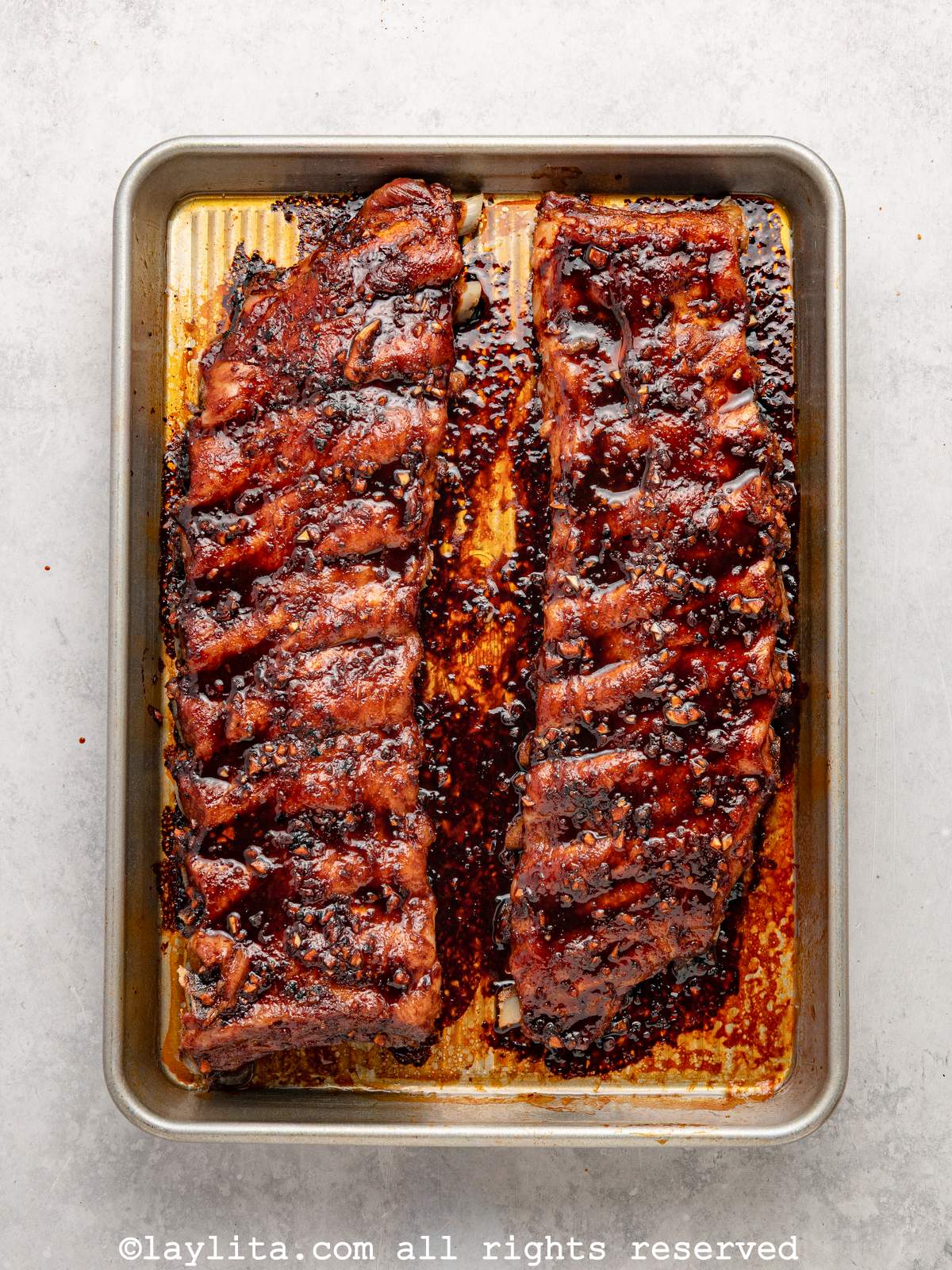 Overhead shot of two racks of sticky pork ribs on a sheet pan