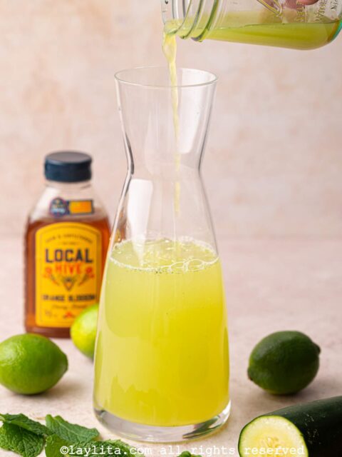 Cucumber lime mint agua fresca mix being poured into a glass pitcher