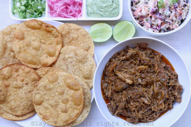 View of several corn tostadas, a bowl of pulled pork and toppings on a white tray