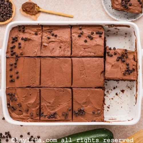 Overhead view of a chocolate zucchini cake in a baking dish cut into slices with a few slices missing.
