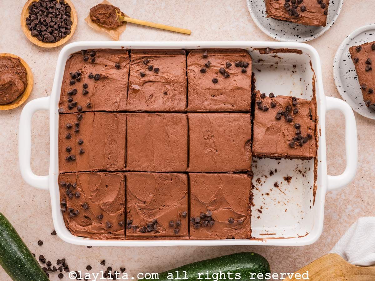 Overhead view of a chocolate zucchini cake in a baking dish cut into slices with a few slices missing.