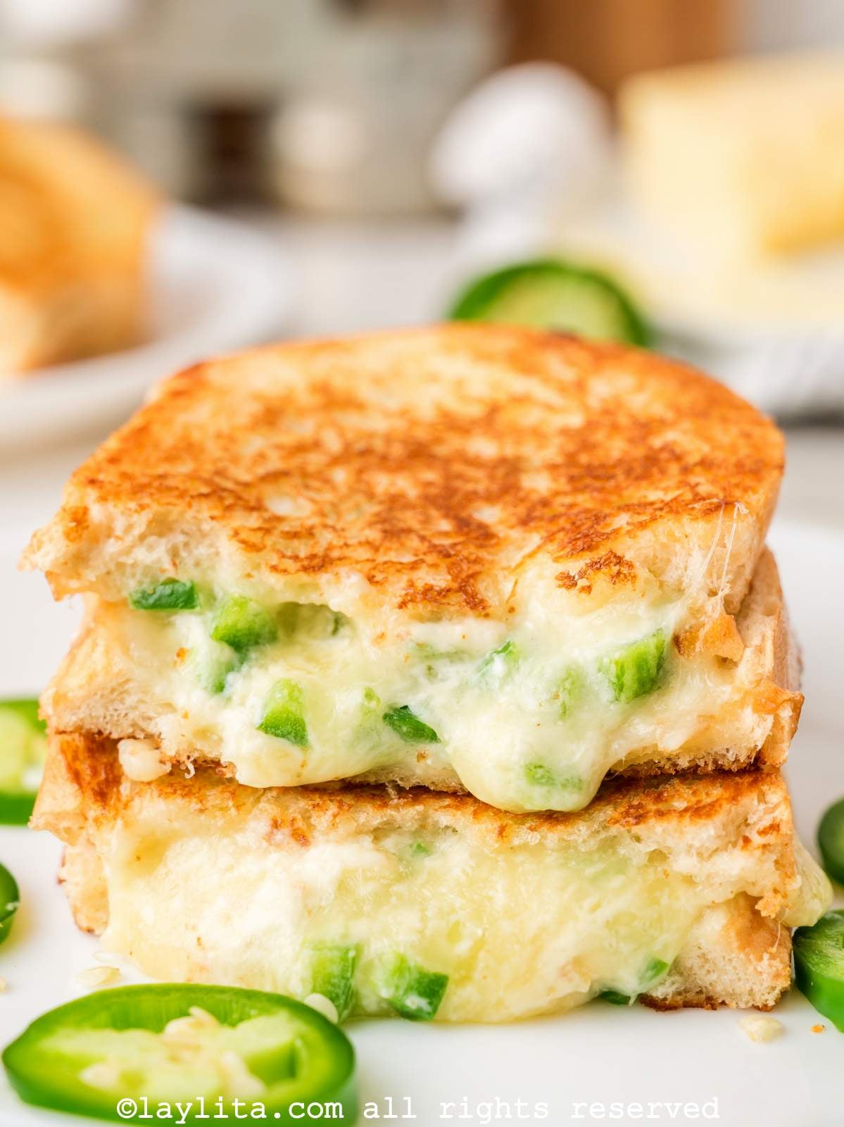 Two halves of a grilled jalapeño cheese sandwich on top of each other on a plate.