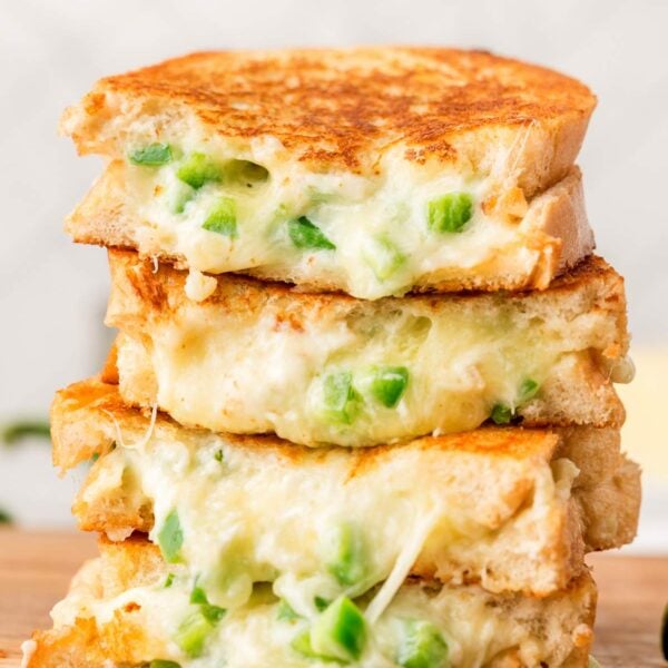 Four slices of jalapeño popper grilled cheese stacked on top of each other on a wooden board.