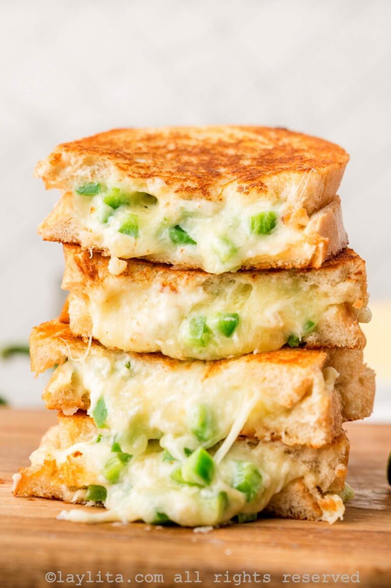Four slices of jalapeño popper grilled cheese stacked on top of each other on a wooden board.