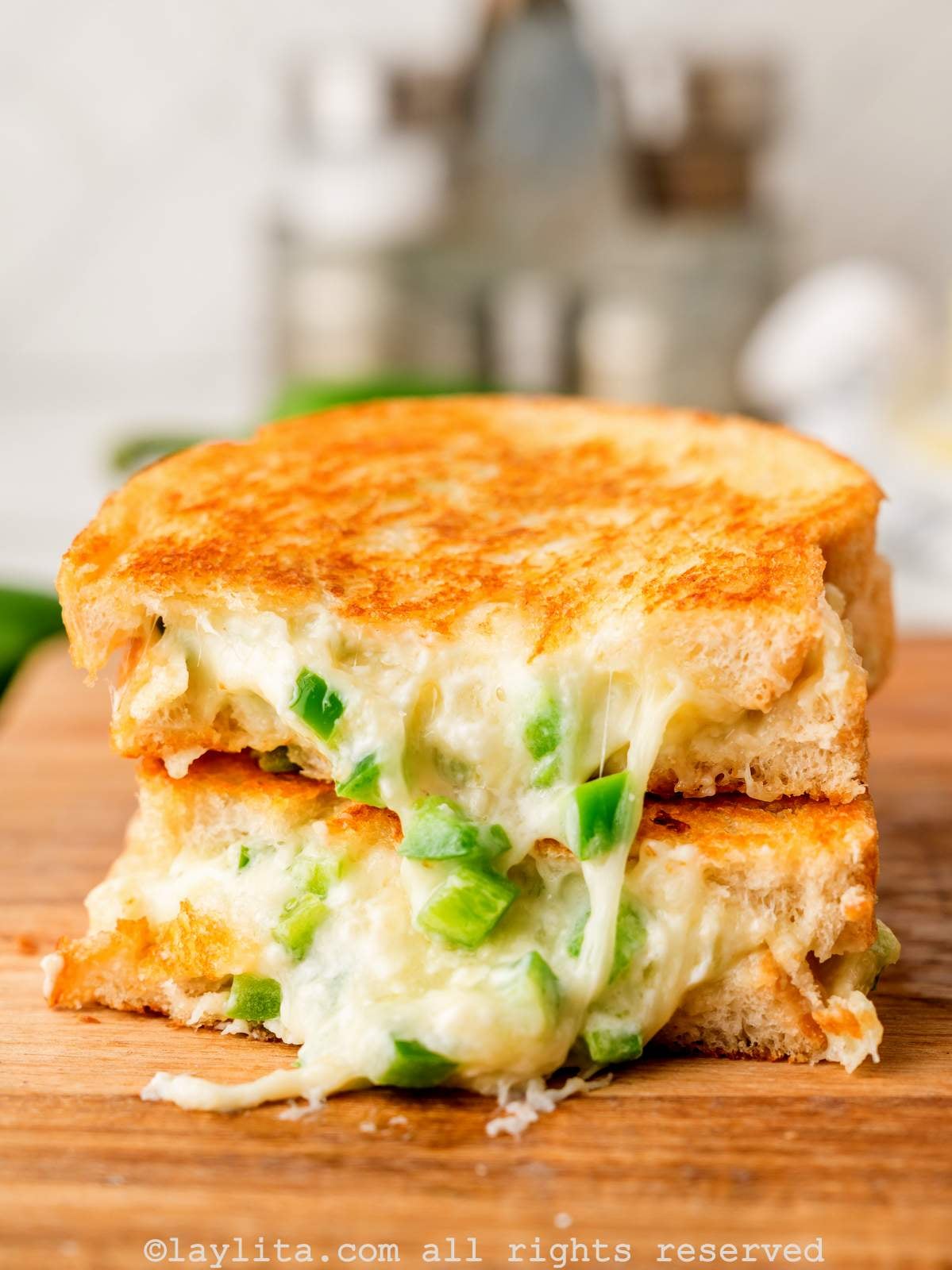 Two slices of grilled cheese sandwiches with cheese and pieces of jalapeños oozing out on a wooden board