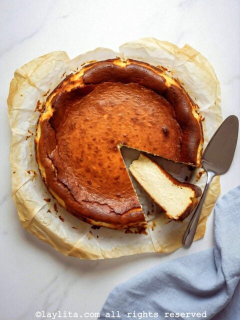 Overhead shot of a basque cheesecake on parchment paper with one slice on its side and a serving spatula next to it