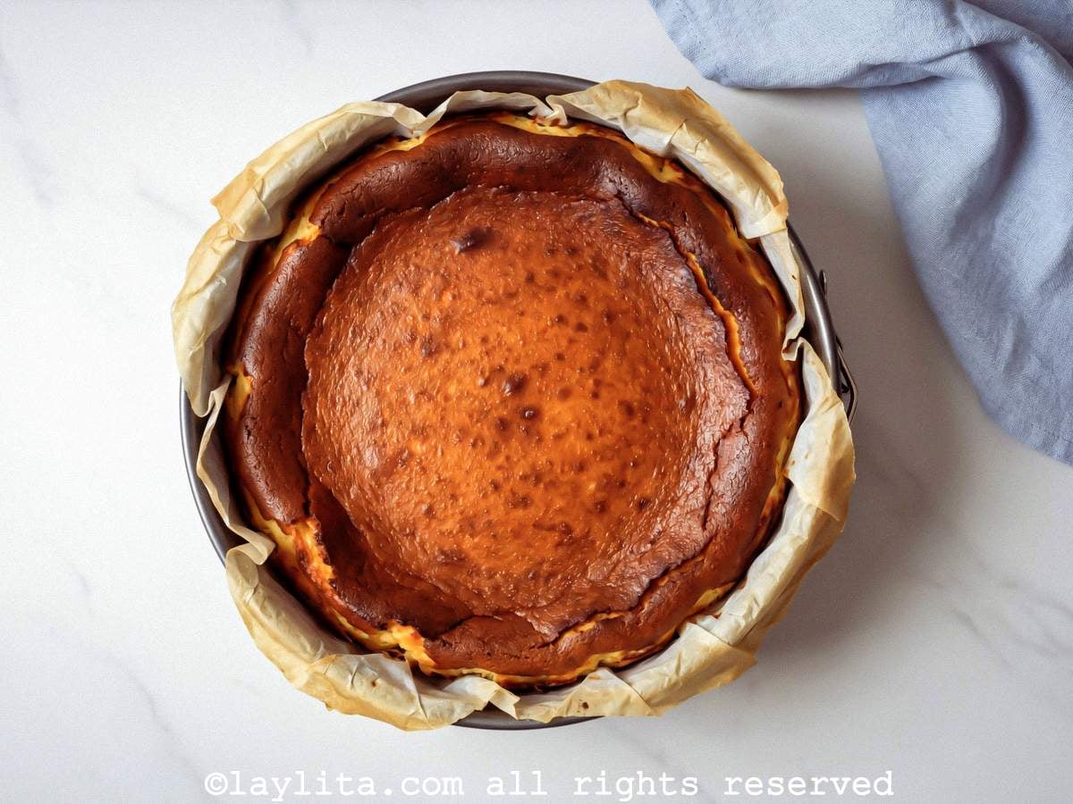 Overhead view of a baked basque cheesecake in a cake pan on a countertip next to a light blue kitchen towel