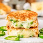 Side view of a jalapeno popper grilled cheese stack on top of each other on a white plate.