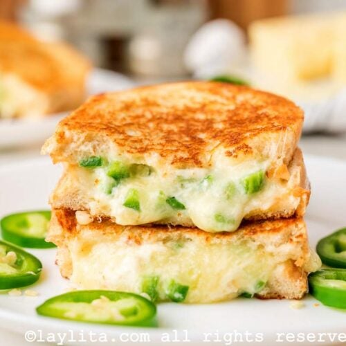 Side view of a jalapeno popper grilled cheese stack on top of each other on a white plate.