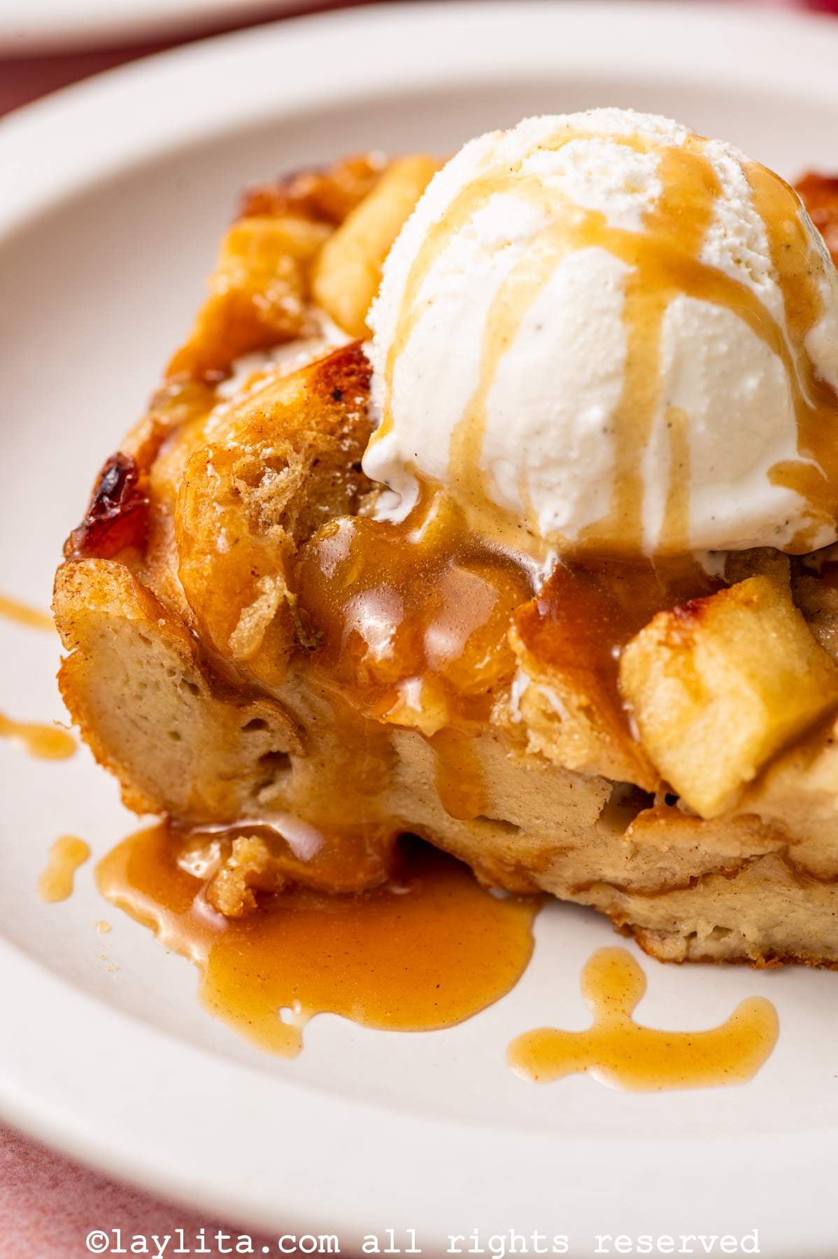 Closeup view of a portion of apple bread pudding topped with ice cream and salted caramel sauce