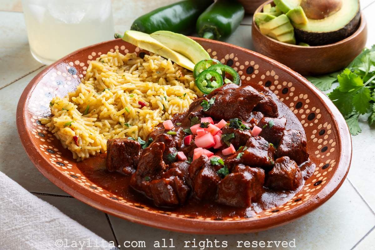 Side view of a platter of Mexican rice with beef chili colorado topped with pickled radishes and cilantro