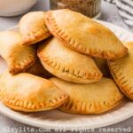 A white plate fill of sweet potato empanadas, with a striped kitchen towel on the side