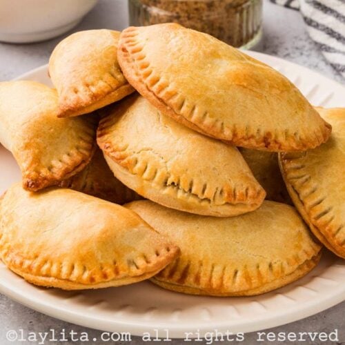 A white plate fill of sweet potato empanadas, with a striped kitchen towel on the side