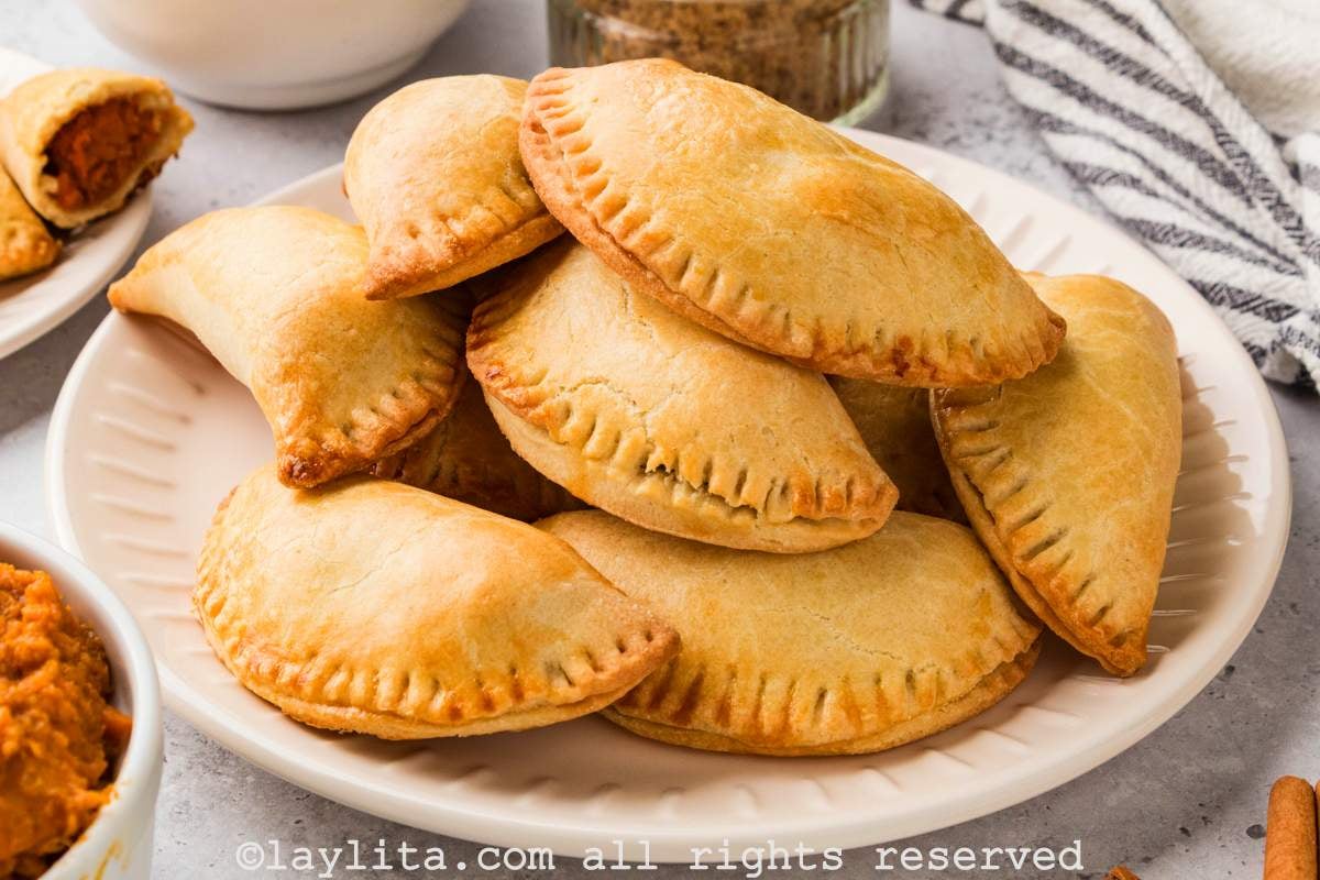 A white plate fill of sweet potato empanadas, with a striped kitchen towel on the side