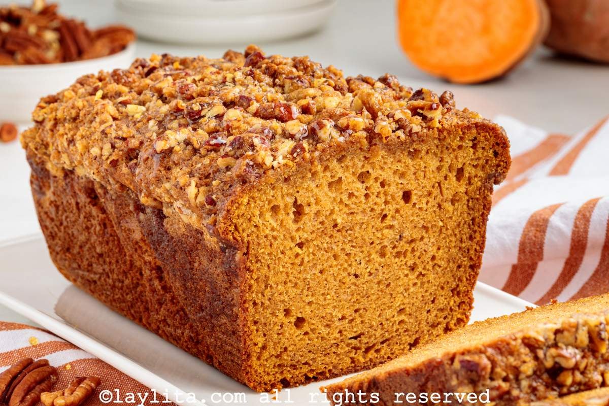 Side view of a sweet potato loaf cake topped with pecan streusel on a white plate, with a slice cut off