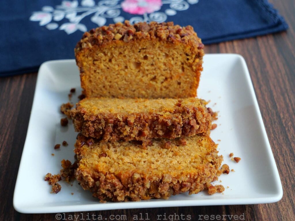A sweet potato loaf cake on a white plate, with a couple of slices already cut, with a blue floral kitchen towel in the background