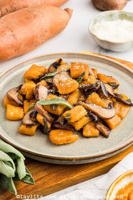 Sideview of a brown plate filled with sweet potato gnocchi sauteed with mushrooms