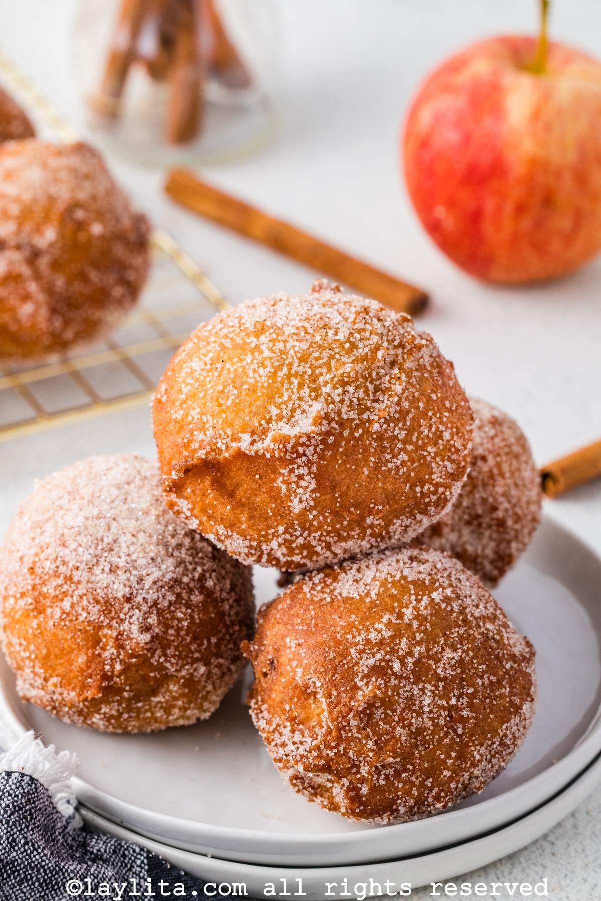 Four apple buñuelos covered in cinnamon sugar piled on a plate