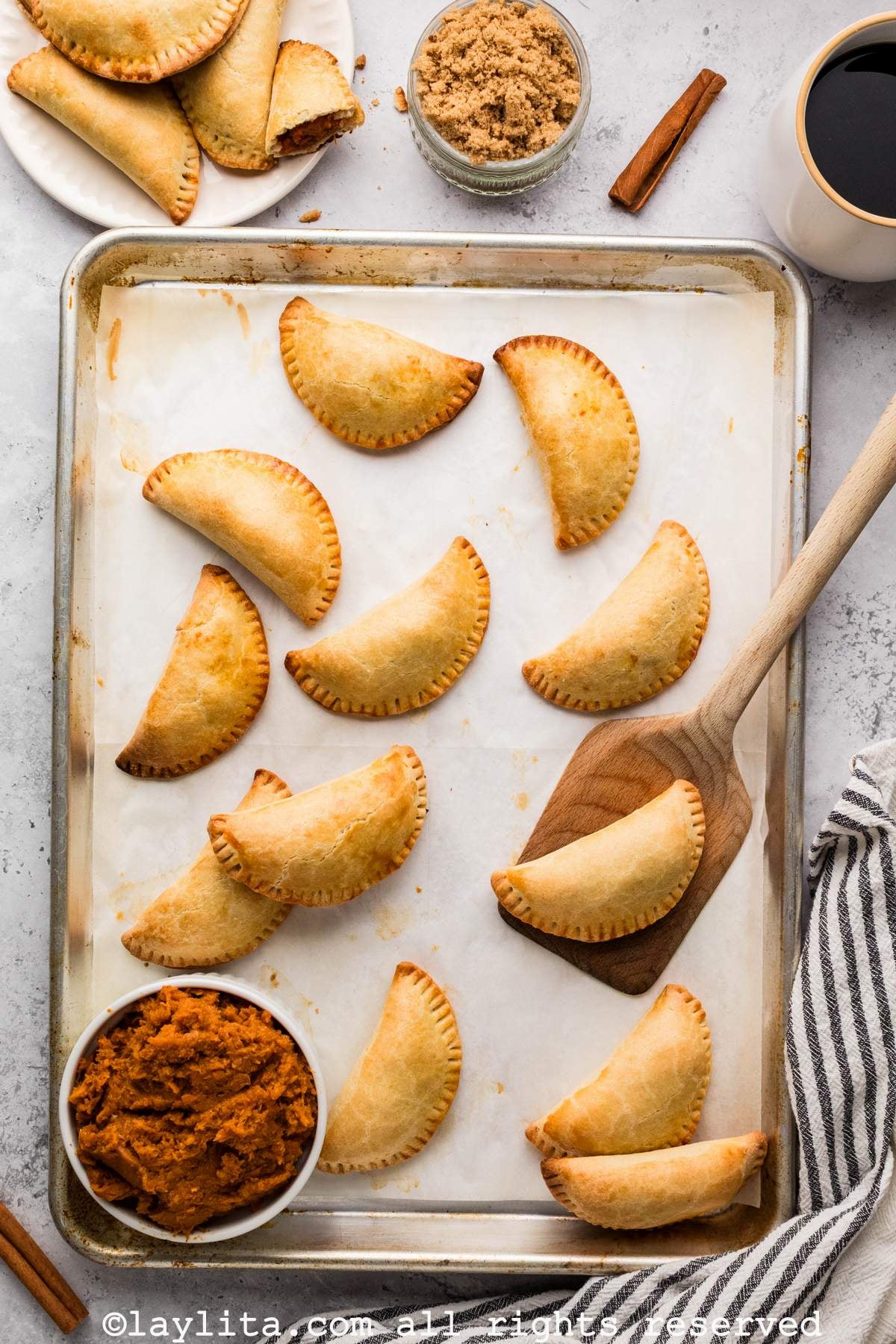 Overhead view of a tray full of sweet potato empanads, with a spatula holding one